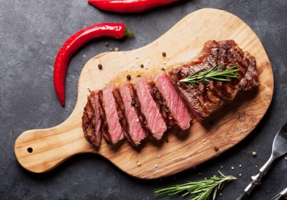 A steak on a cutting board with some red peppers